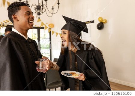 Graduates in caps and gowns celebrating with snacks and drinks at party 135636100
