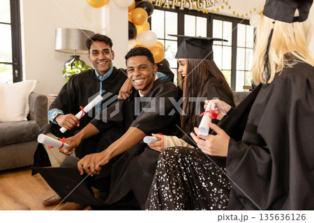Graduates in caps and gowns celebrating success with diplomas at home 135636126