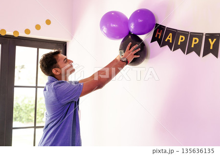 Man decorating wall with purple balloons and banner for celebration at home Man decorating wall with purple balloons and banner for celebration at home 135636135