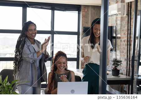 Celebrating success, diverse women cheering and clapping around laptop in office Celebrating success, diverse women cheering and clapping around laptop in office 135636164