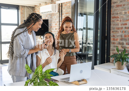 In office, diverse businesswomen cheering around laptop, celebrating success together 135636178