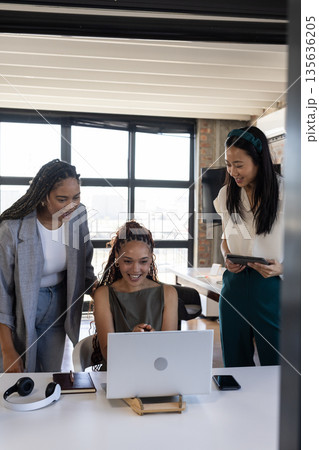 Diverse business team celebrating success while looking at laptop in modern office Diverse business team celebrating success while looking at laptop in modern office 135636205