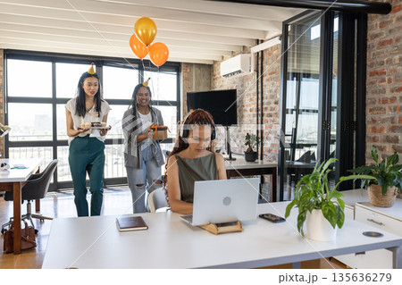 Colleagues surprising woman with cake and balloons in modern office celebration 135636279