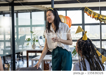 Celebrating in office, businesswoman holding glass with colleagues, smiling happily Celebrating in office, businesswoman holding glass with colleagues, smiling happily 135636326