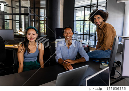Smiling business team collaborating at office desk with laptops and documents Smiling business team collaborating at office desk with laptops and documents 135636386