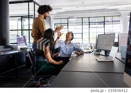 Business team celebrating success at office desk with high fives and laughter Business team celebrating success at office desk with high fives and laughter 135636412