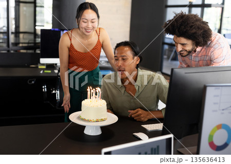 Colleagues celebrating birthday in office, man blowing out candles on cake Colleagues celebrating birthday in office, man blowing out candles on cake 135636413