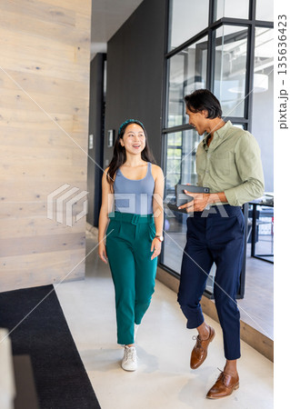 Asian colleagues walking in modern office, discussing work with smiles 135636423
