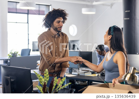 In modern office, colleagues shaking hands, celebrating successful work collaboration 135636439
