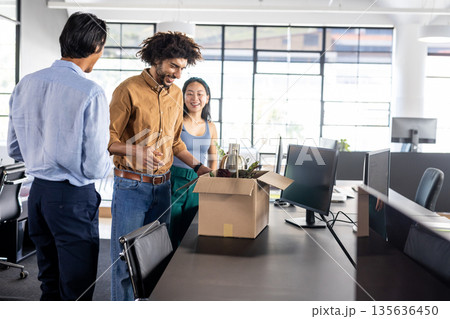Colleagues unpacking welcome gift box in modern office, smiling and chatting 135636450