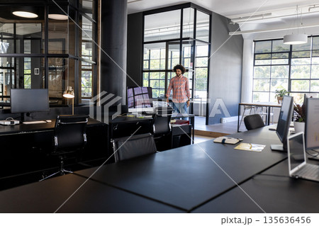 Businessman entering modern office with large windows and multiple computer screens 135636456