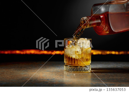 Whiskey is poured into a glass with ice. 135637053