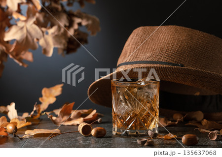Whiskey with ice on a stone table with dried oak leaves. Whiskey with ice on a stone table with dried oak leaves. 135637068