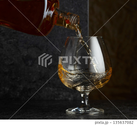 Pouring brandy from a bottle into a glass. 135637082