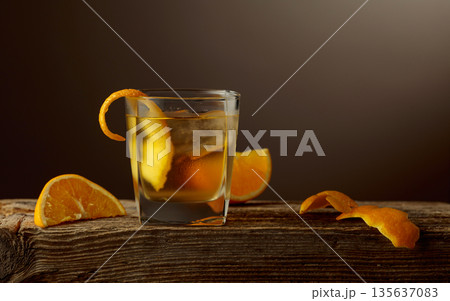 Old Fashioned cocktail with a ice, garnished with an orange peel on a old wooden board. 135637083