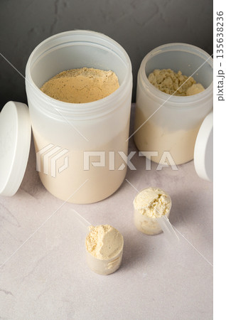 Protein powder in scoops with white plastic protein tubes, jars in background. Body building, muscle growth and food supplement concept 135638236