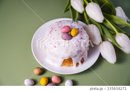 Easter spring cake with chocolate mini eggs, wooden bunny and white tulip flowers. Green background. Copy space 135638271
