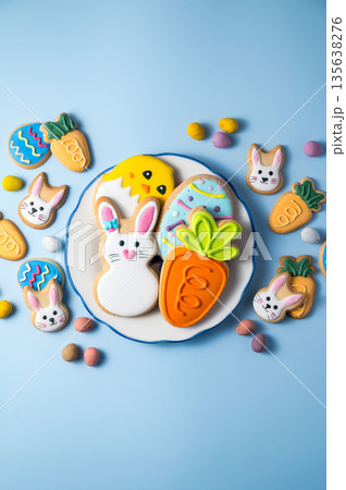 Easter holiday background with easter cookies in a plate: bunny, chick, carrot and egg on blue background, with mini chocolate egg candies Easter holiday background with easter cookies in a plate: bunny, chick, carrot and egg on blue background, with mini chocolate egg candies 135638276