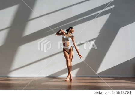 Shadow of the windows, sunlight, standing. Beautiful young woman with slim body type is indoors Shadow of the windows, sunlight, standing. Beautiful young woman with slim body type is indoors 135638781
