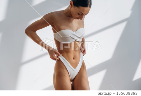 Showing abs, standing. Beautiful young woman with slim body type is indoors Showing abs, standing. Beautiful young woman with slim body type is indoors 135638865