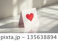 White folded card displaying a red heart against a light background with shadows 135638894