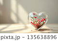 Heart glass vase holding small red and pink flowers blooming inside 135638896