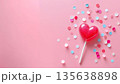 Pink heart lollipop with colorful confetti scattered across a vibrant background 135638898