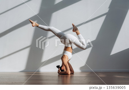 Headstand, doing exercise. Beautiful young woman with slim body type is indoors 135639005