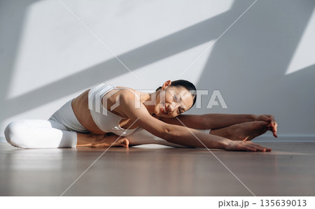 Professional yoga exercises. Beautiful young woman with slim body type is indoors Professional yoga exercises. Beautiful young woman with slim body type is indoors 135639013