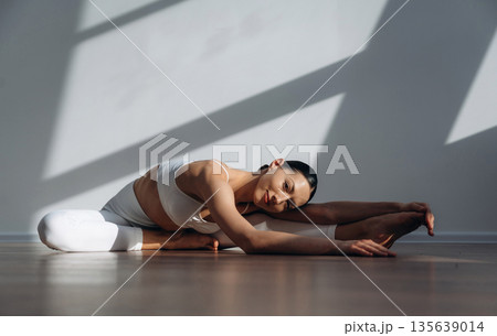 Professional yoga exercises. Beautiful young woman with slim body type is indoors Professional yoga exercises. Beautiful young woman with slim body type is indoors 135639014