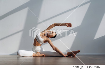 On the floor, doing yoga sport exercises. Beautiful young woman with slim body type is indoors 135639020