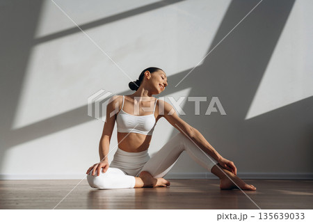 Smiling, sitting on the floor. Beautiful young woman with slim body type is indoors 135639033