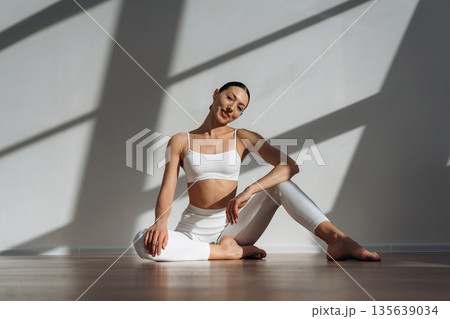 Smiling, sitting on the floor. Beautiful young woman with slim body type is indoors 135639034