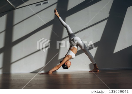 Legs are stretching, yoga exercise. Beautiful young woman with slim body type is indoors Legs are stretching, yoga exercise. Beautiful young woman with slim body type is indoors 135639041