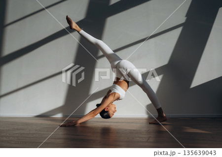 Legs are stretching, yoga exercise. Beautiful young woman with slim body type is indoors Legs are stretching, yoga exercise. Beautiful young woman with slim body type is indoors 135639043