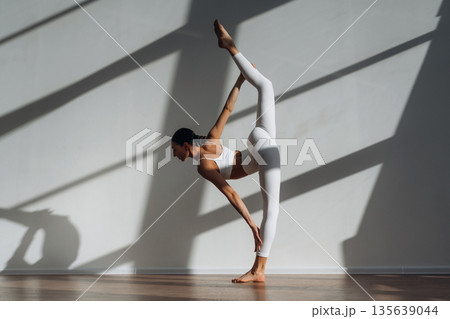 Legs are stretching, yoga exercise. Beautiful young woman with slim body type is indoors Legs are stretching, yoga exercise. Beautiful young woman with slim body type is indoors 135639044