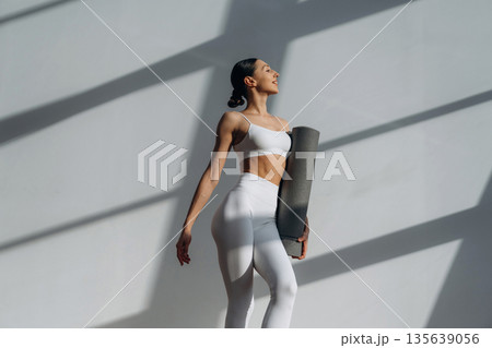 Ready for the session, holding yoga mat. Beautiful young woman with slim body type is indoors 135639056