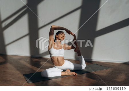 Health care, physical activity, sitting on the floor. Beautiful young woman with slim body type is indoors Health care, physical activity, sitting on the floor. Beautiful young woman with slim body type is indoors 135639119