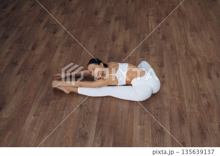 Enjoying doing yoga. Beautiful young woman with slim body type is indoors Enjoying doing yoga. Beautiful young woman with slim body type is indoors 135639137