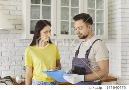 Repairman in uniform giving woman client contract for repair to sign after finished work 135640476