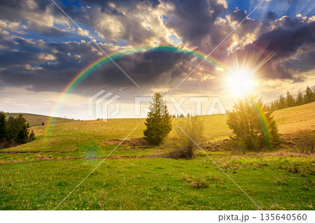 rolling hill with green field under cloudy sky in spring at sunset. scenic view countryside landscape mountains in evening light. timeless nostalgia book cover with rainbow. natural beauty aesthetic rolling hill with green field under cloudy sky in spring at sunset. scenic view countryside landscape mountains in evening light. timeless nostalgia book cover with rainbow. natural beauty aesthetic 135640560