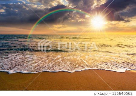 sand beach at the sea for summer vacation concept. beautiful sunset at perfect coast with calm waves and clouds on sky in evening light. scenic landscape for timeless nostalgia book cover with rainbow 135640562