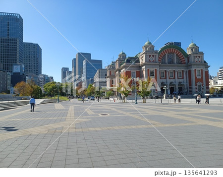 灰色とベージュのブロックタイルの広場の向こうに都会のビル群を背景に建つ赤レンガの古い建物 135641293