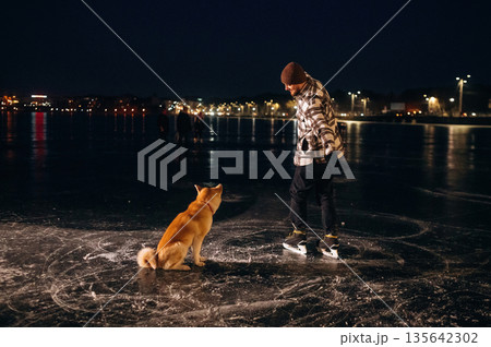 Breed of Akita Inu. Man with dog is on the ice with skates in winter Breed of Akita Inu. Man with dog is on the ice with skates in winter 135642302