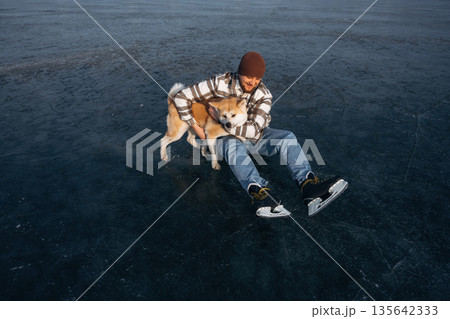 Lovely moments with cute pet. Man with Akita Inu dog is on the ice with skates in winter 135642333