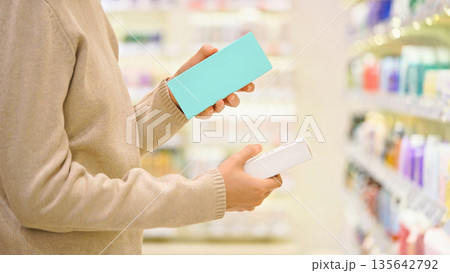 Woman reading and examines ingredient labels while comparing and choosing between cosmetic products in a beauty store aisle, focusing on making an informed decision. Woman reading and examines ingredient labels while comparing and choosing between cosmetic products in a beauty store aisle, focusing on making an informed decision. 135642792