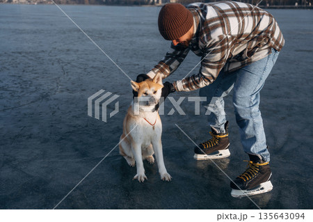 Human's best friend. Man with Akita Inu dog is on the ice with skates in winter Human's best friend. Man with Akita Inu dog is on the ice with skates in winter 135643094