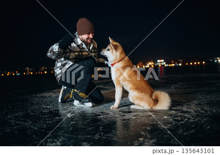 Training the tricks, giving paw. Man with Akita Inu dog is on the ice with skates in winter 135643101