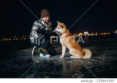 Man with Akita Inu dog is on the ice with skates in winter 135643103