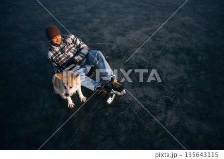 Dark ice, top view. Man with Akita Inu dog is on the ice with skates in winter Dark ice, top view. Man with Akita Inu dog is on the ice with skates in winter 135643115